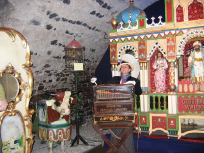 экскурсовод, одетая в старинный костюм, демонстирует работу шарманки